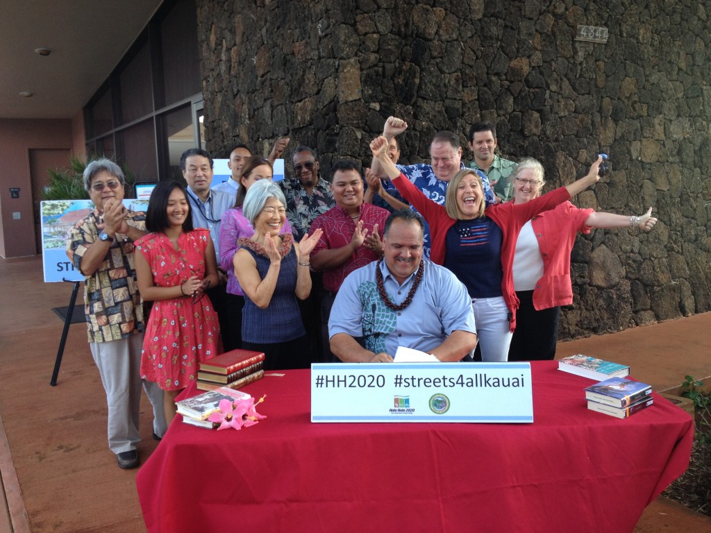A group of county officials and personnel along with community members enthusiastically applaud as Mayor Bernard Carvalho, Jr. signs the Complete Streets bill. From left: Deputy County Engineer Lyle Tabata; Marisa Valenciano, TVR permit enforcement research specialist; Peter Nakamura, county planner; Kevin Santiago, summer intern; Marie Williams, county planner; Councilwoman JoAnn Yukimura; Neil Clendeninn, Lîhu'e Business Association; Planning Director Michael Dahilig; Lee Steinmetz, transportation planner; Councilman Tim Bynum; Bev Brody, Get Fit Kaua'i director; Ian Jung, deputy county attorney; and Carolyn Larson, Lîhu'e Public Library head librarian. 