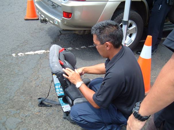 Sgt. Ray Takekawa, a certified Child Passenger Seat Technician, makes the necessary adjustments to a car seat during a free car seat safety inspection.