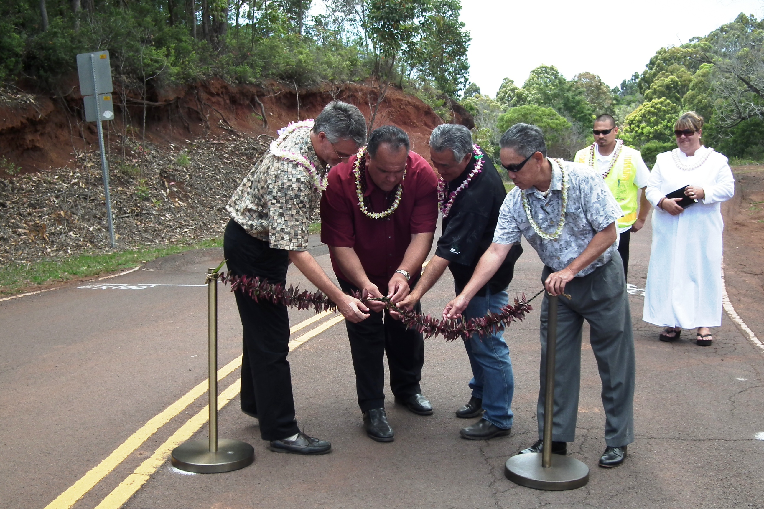 (L To R) County Engineer Larry Dill, Mayor Bernard Carvalho, Jr., Norman Shinno, island manager with Grace Pacific Corp, and County Councilman Dickie Chang untie the traditional lei following a blessing that marked the start of the Kokee Road enhancement project, while project manager Marween Ibanez and Kahu Jade Battad look on.